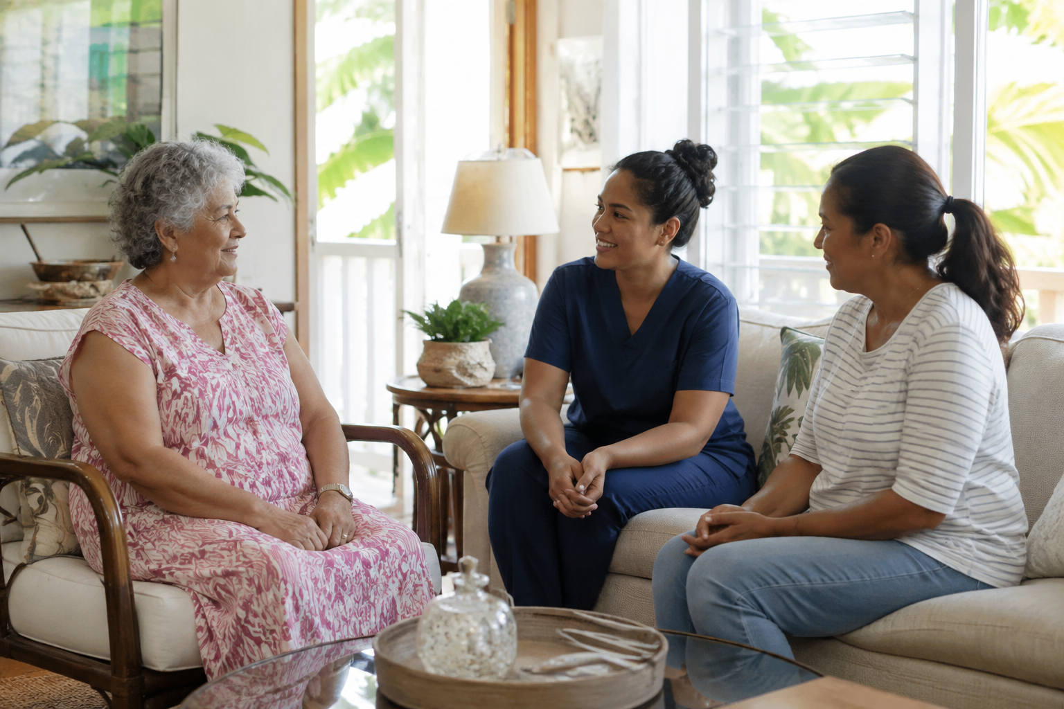 An older woman talks with two women, one wearing scrubs, in a living room.