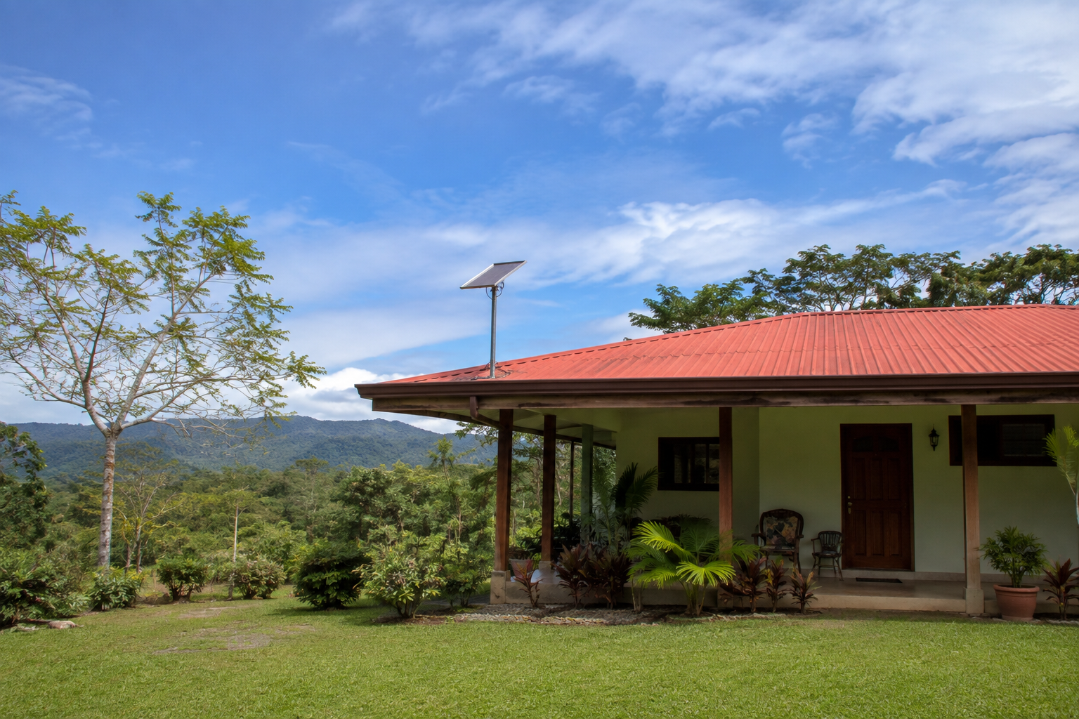 A rectangular antenna mounted above a low-rise home with a tropical garden and open sky.