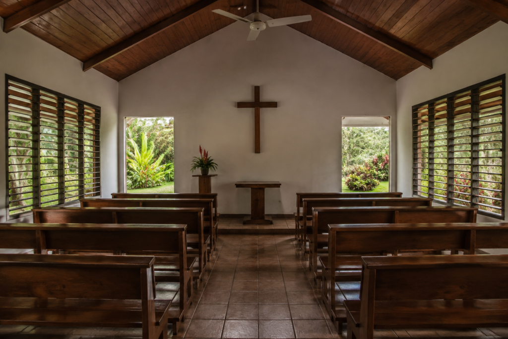 Wooden pews face a plain cross in a small church.