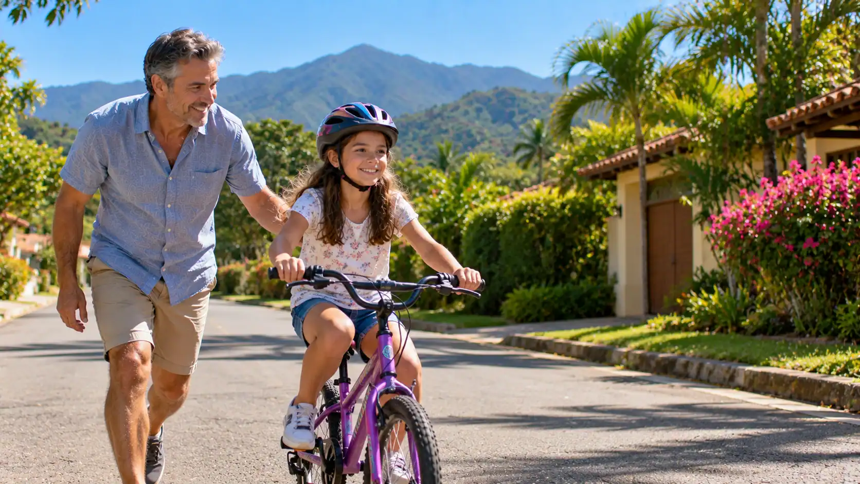 A stepfather teaching his stepdaughter to ride a bicycle on a quiet Costa Rican street