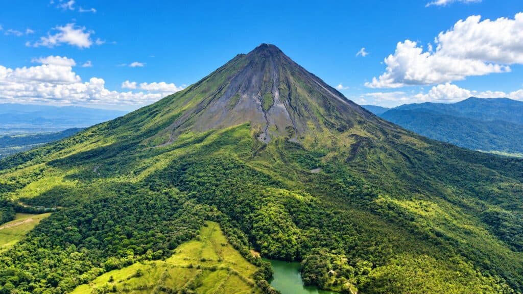 Arenal Volcano cone rising above green rainforest and a small lake in Costa Rica