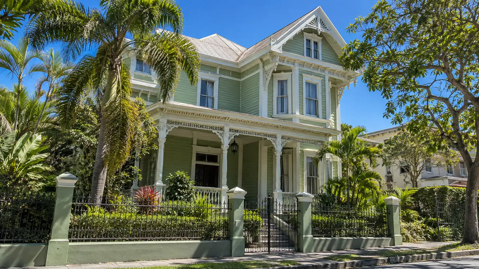 A restored Victorian-style wooden house painted pale green with white trim and a front porch on a tree-lined street in Barrio Amón, San José
