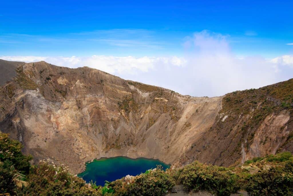 Irazú Volcano crater with its green lake and steep brown walls under a blue sky in Cartago