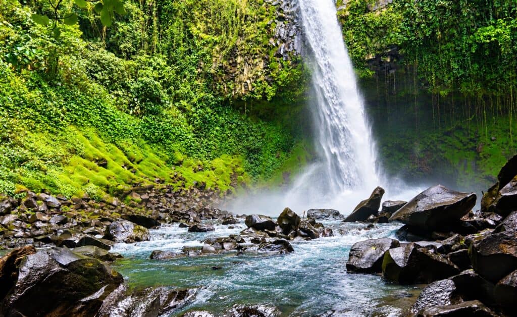 La Fortuna Waterfall plunging from a basalt cliff into a rocky river near Arenal, Costa Rica