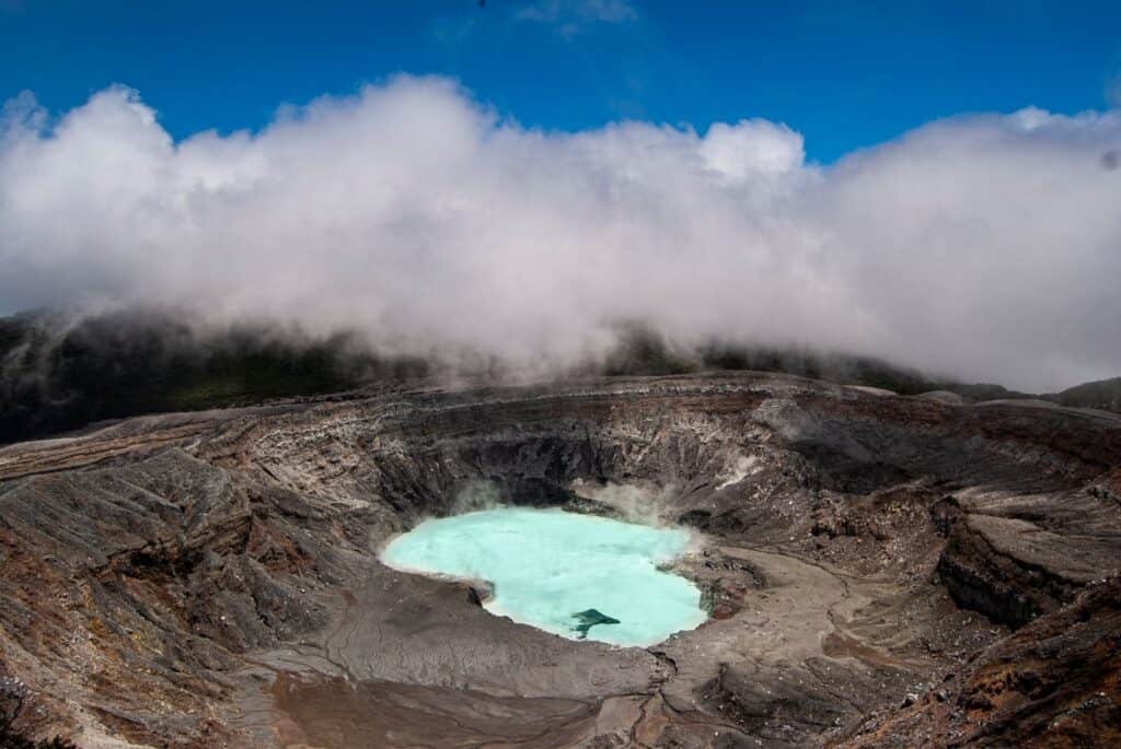 Poás Volcano crater in Costa Rica with its turquoise acid lake and steam under a blue sky